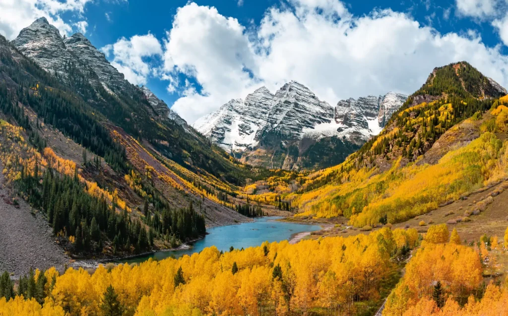Autumn colors blanket mountainside around serene alpine lake and maroon Bells in Colorado during fall season